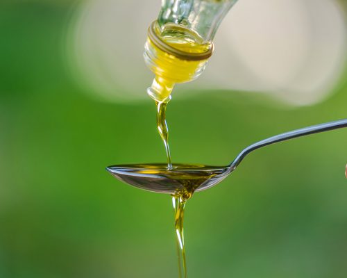 Pouring Olive oil into spoon on Green park garden background
